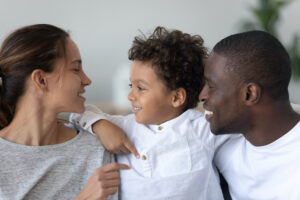Smiling young multiethnic parents hug cuddle with cute little biracial son at home, loving international family have fun playing with small mixed race ethnicity boy child, enjoy weekend together